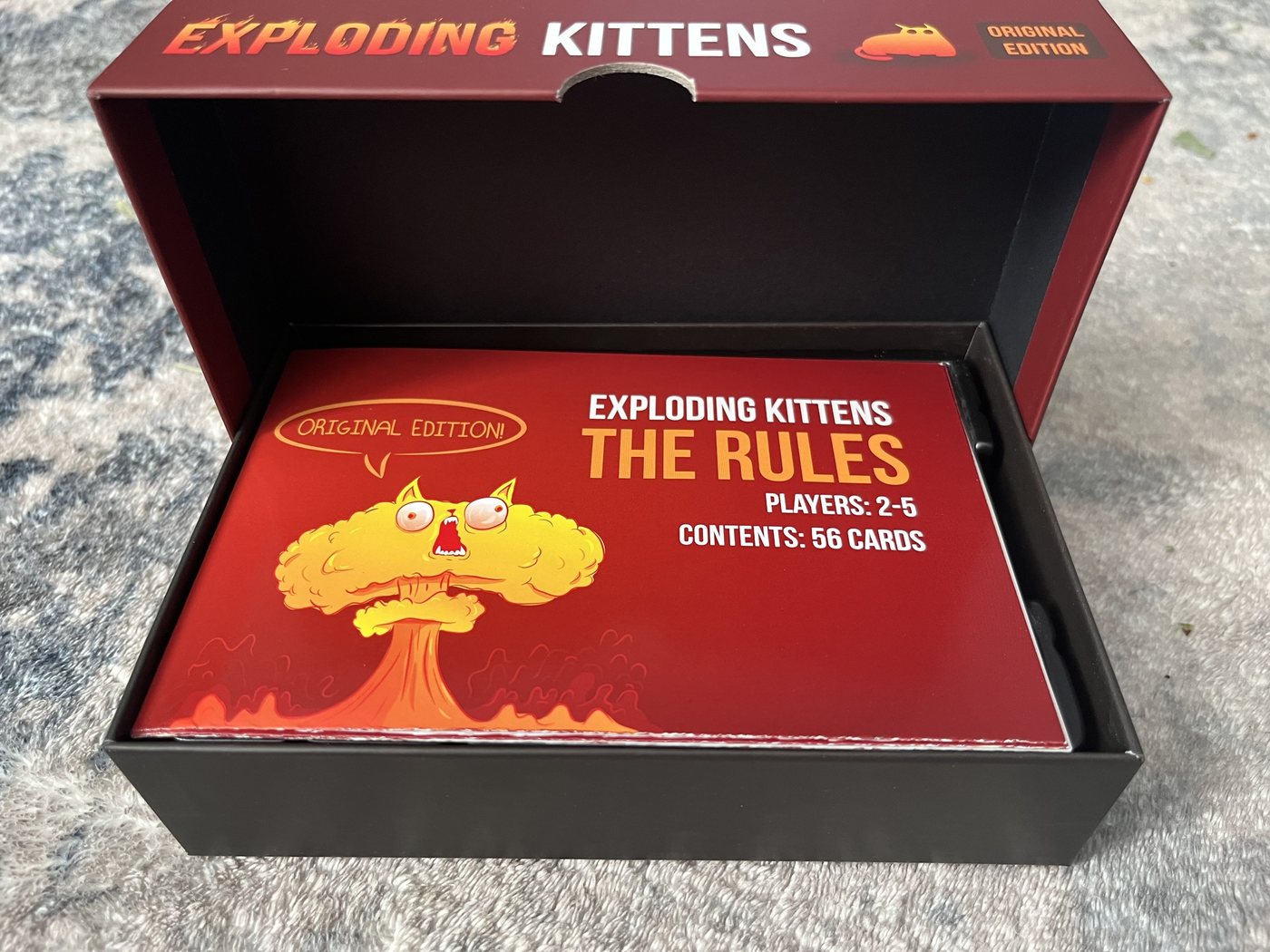 Open Exploding Kittens Original Edition box with the rule sheet on top reading Players 2-5, Contents 56 cards