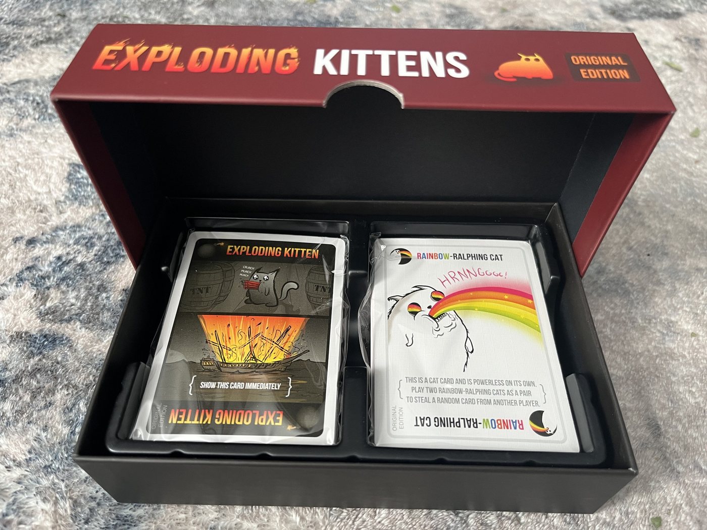 Open Exploding Kittens Original Edition box showing the 56 cards in two wrapped stacks
