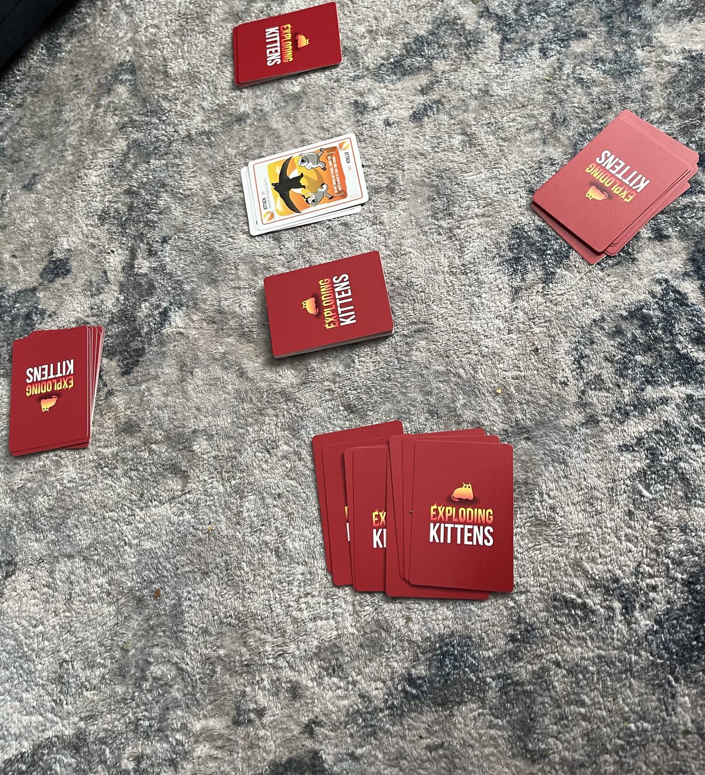 Exploding Kittens set up for four players: four hands around a draw pile and a discard pile