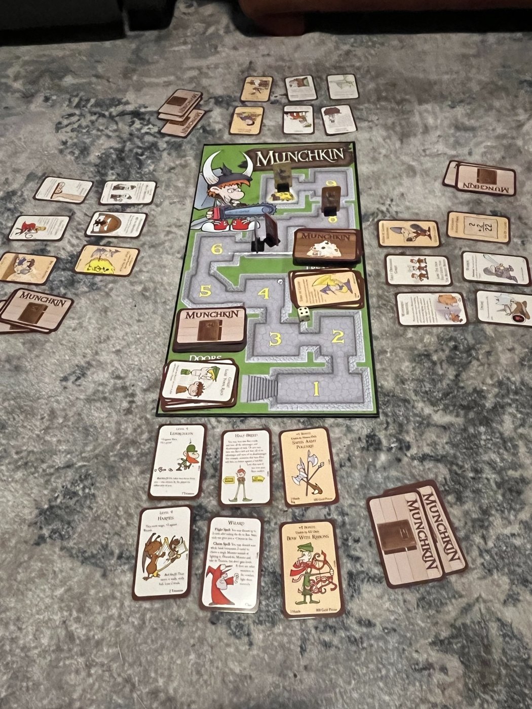 A full game of Munchkin Deluxe set up on our table, with the board in the middle and each player's cards around it