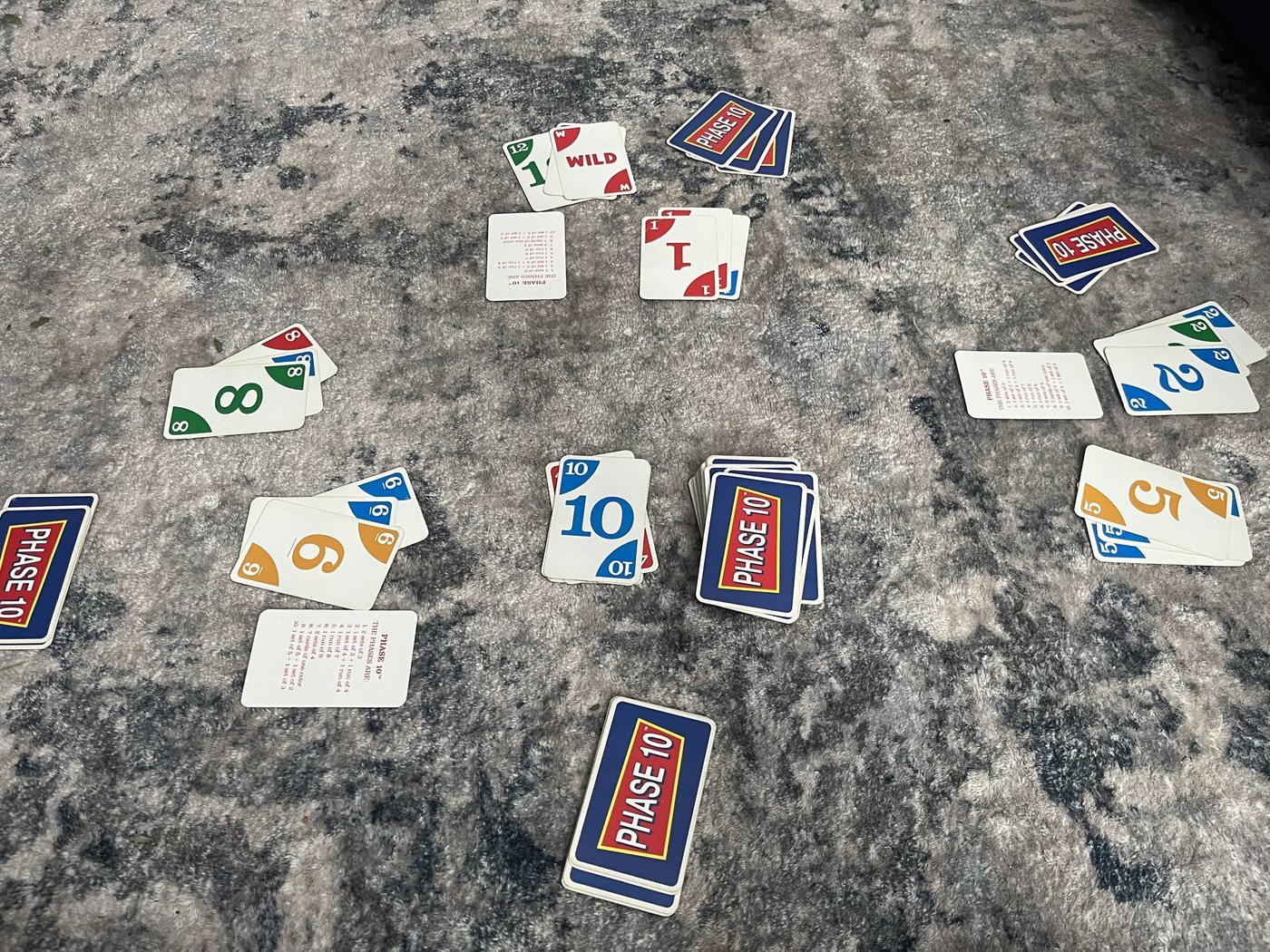 Phase 10 cards dealt out for a round, with hands and reference cards around a draw pile and a discard pile